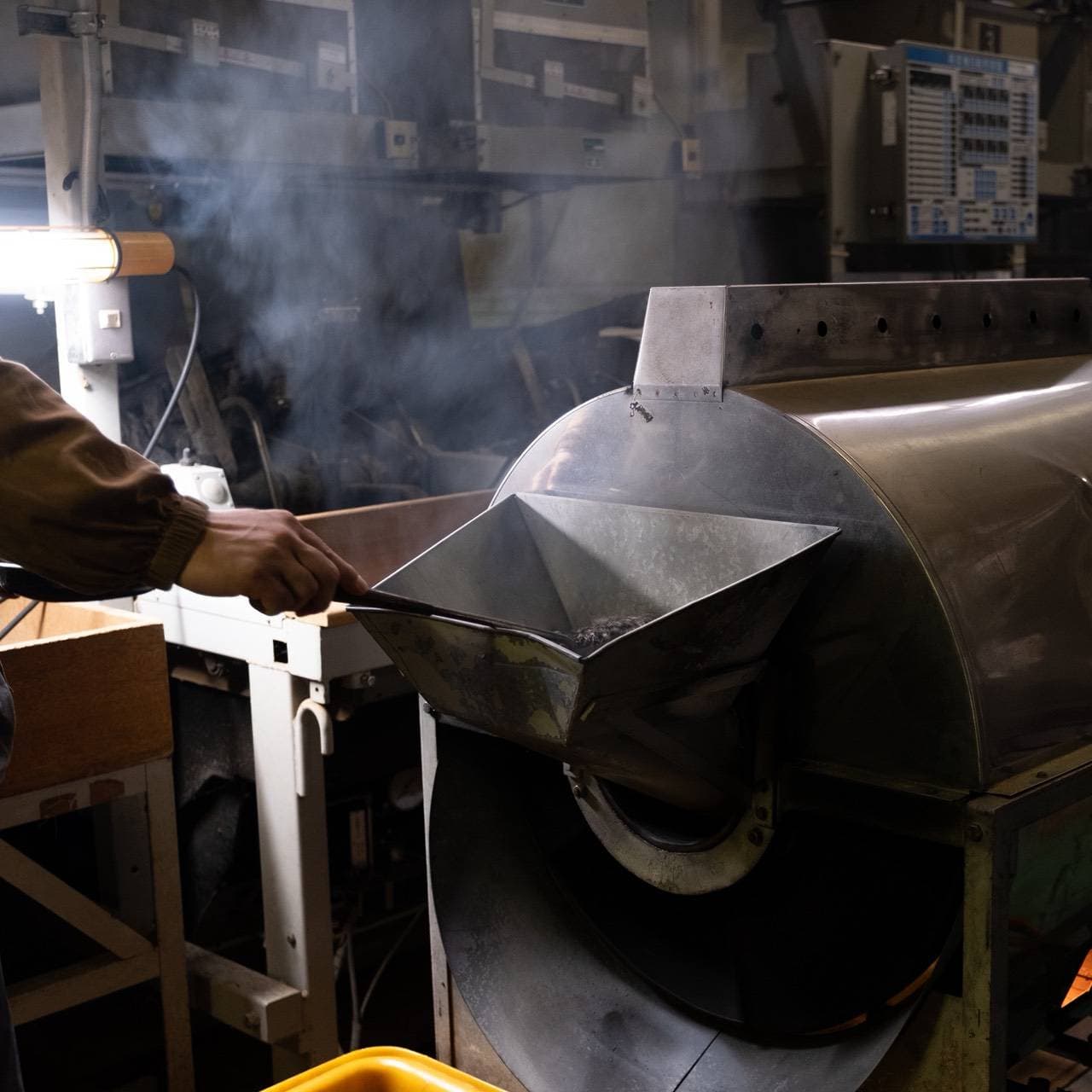 製茶機に茶葉を投入する手、立ち上る湯気